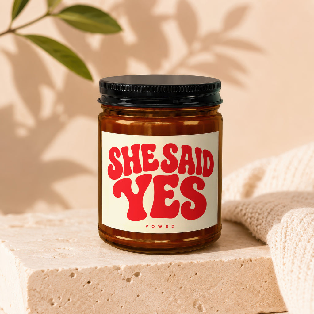 Amber glass candle with white label reading "SHE SAID YES" and "vowed."
