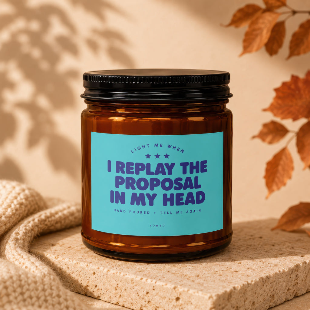Amber glass candle with blue label stating "I replay the proposal in my head."