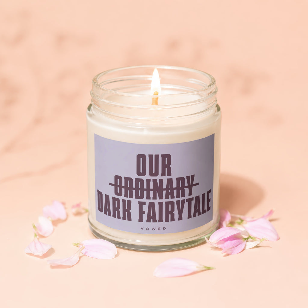 Candle with text "Our Ordinary Dark Fairytale" on a pale pink background with petals.