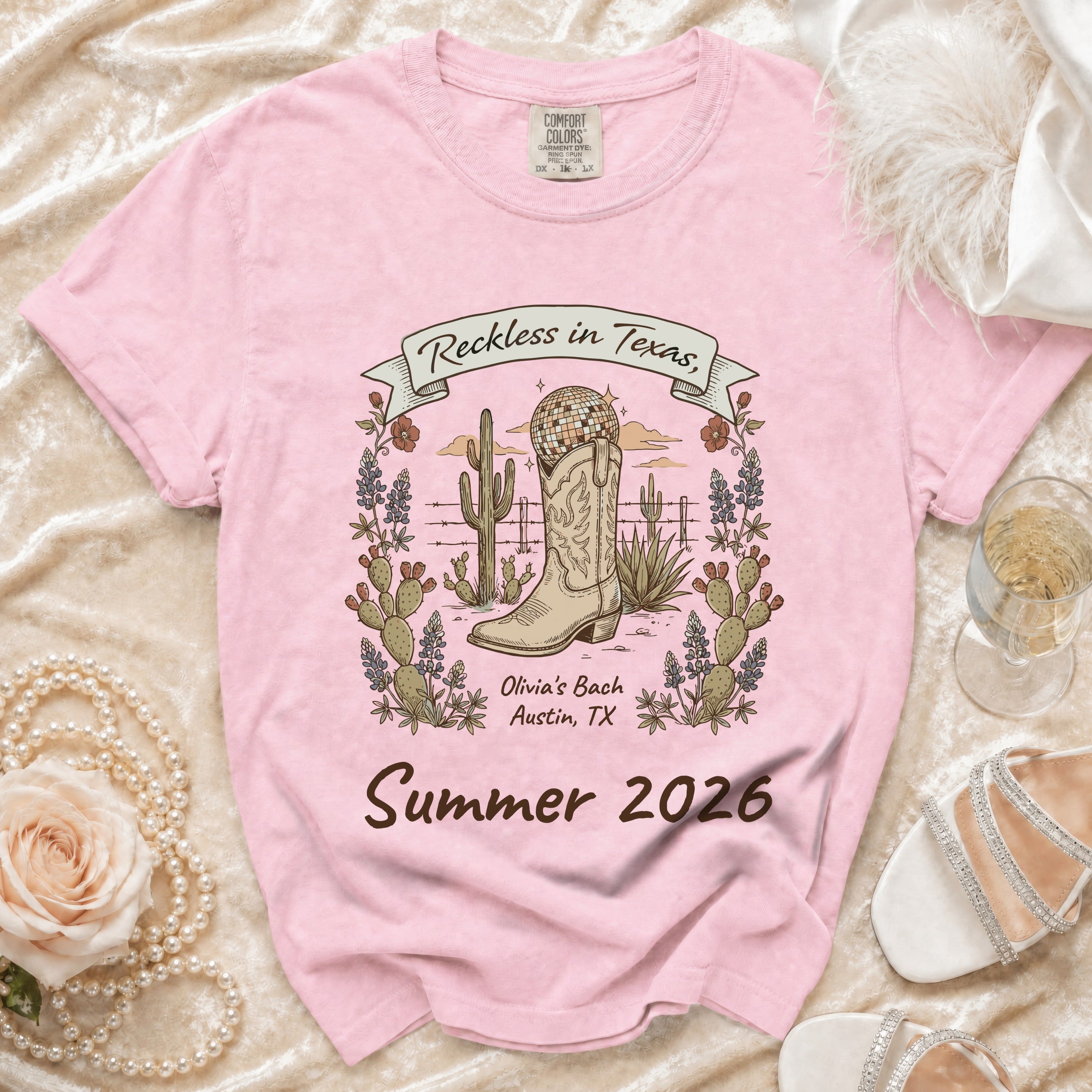 Pink t-shirt with "Reckless in Texas" and desert boot graphic for Summer 2026.