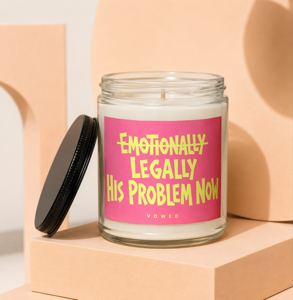 Glass candle with pink label that reads "Emotionally Legally His Problem Now".