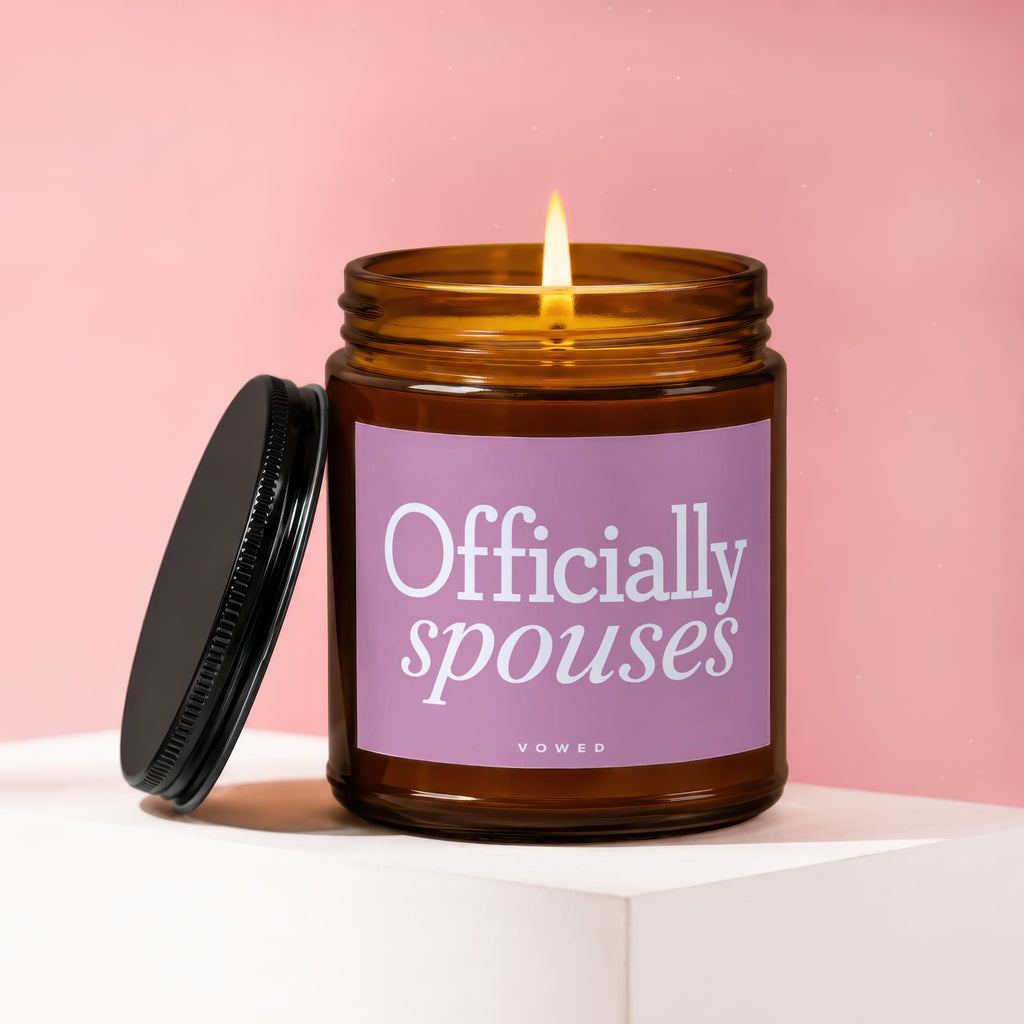 Lit amber glass candle with a pink label reading "Officially spouses" and "vowed".