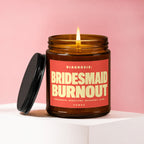 Amber jar candle with lit flame and lid beside it, featuring a coral label.