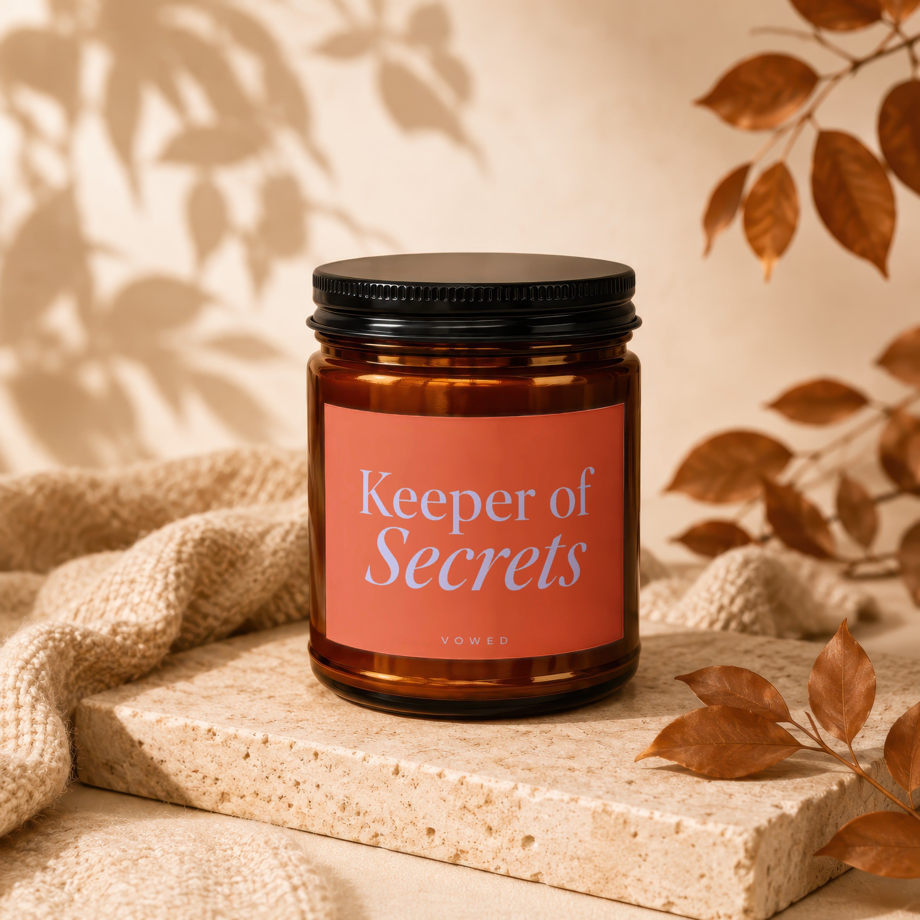 Amber jar candle labeled "Keeper of Secrets" on beige stone with textured fabric.