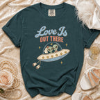 T-shirt with graphic of aliens in a UFO, text "Love Is OUT THERE".