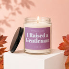 Glass candle with lit wick, purple label reads "Smells Like I Raised a Gentleman".