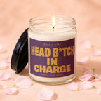 Glass jar candle with lit wick and purple label saying "Smells Like Head B*tch In Charge".