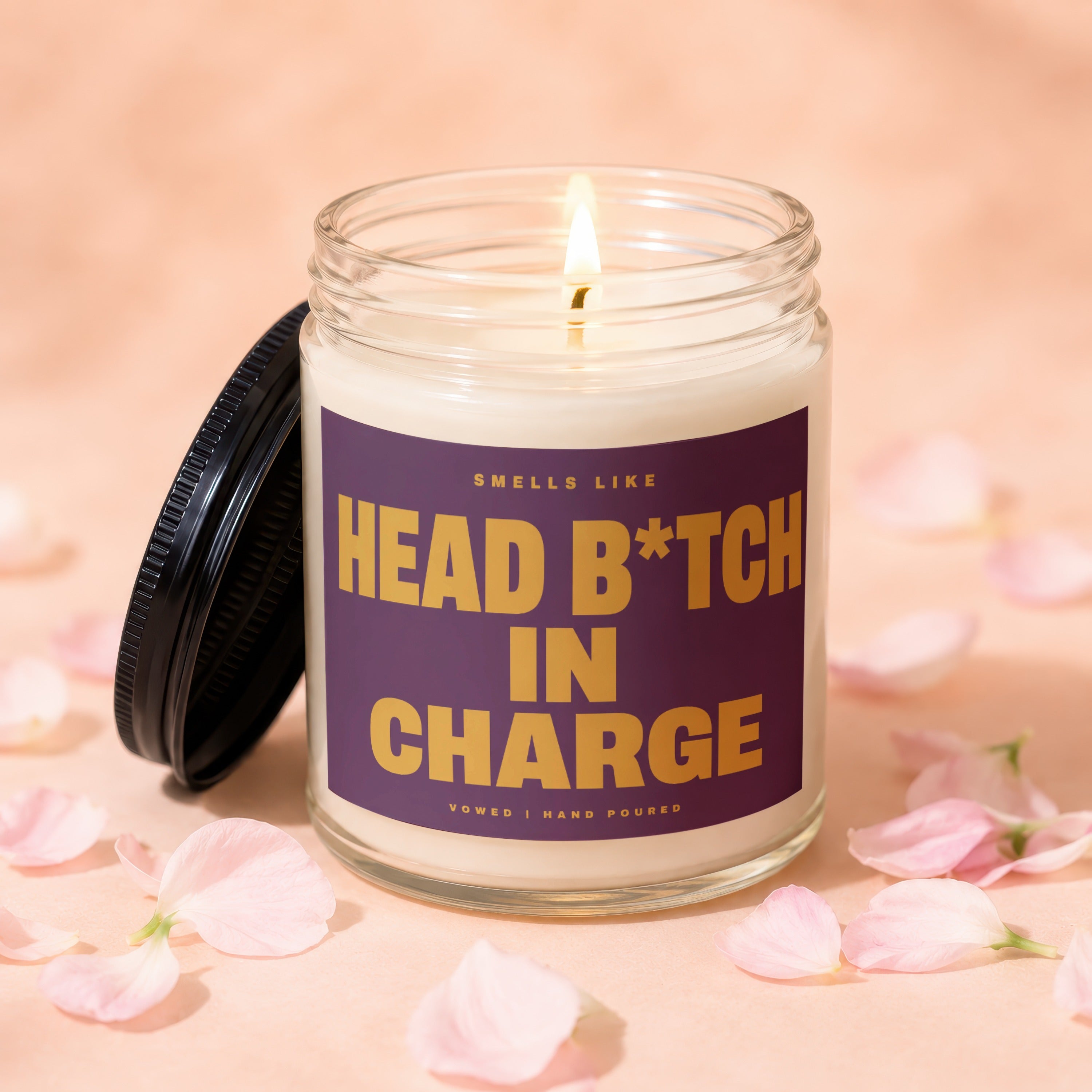 Glass jar candle with lit wick and purple label saying "Smells Like Head B*tch In Charge".