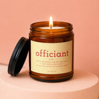 Lit amber jar candle with a cream label reading "officiant" and a definition.