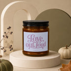 Amber glass candle with black lid featuring "Love, out Loud VOWED" text.