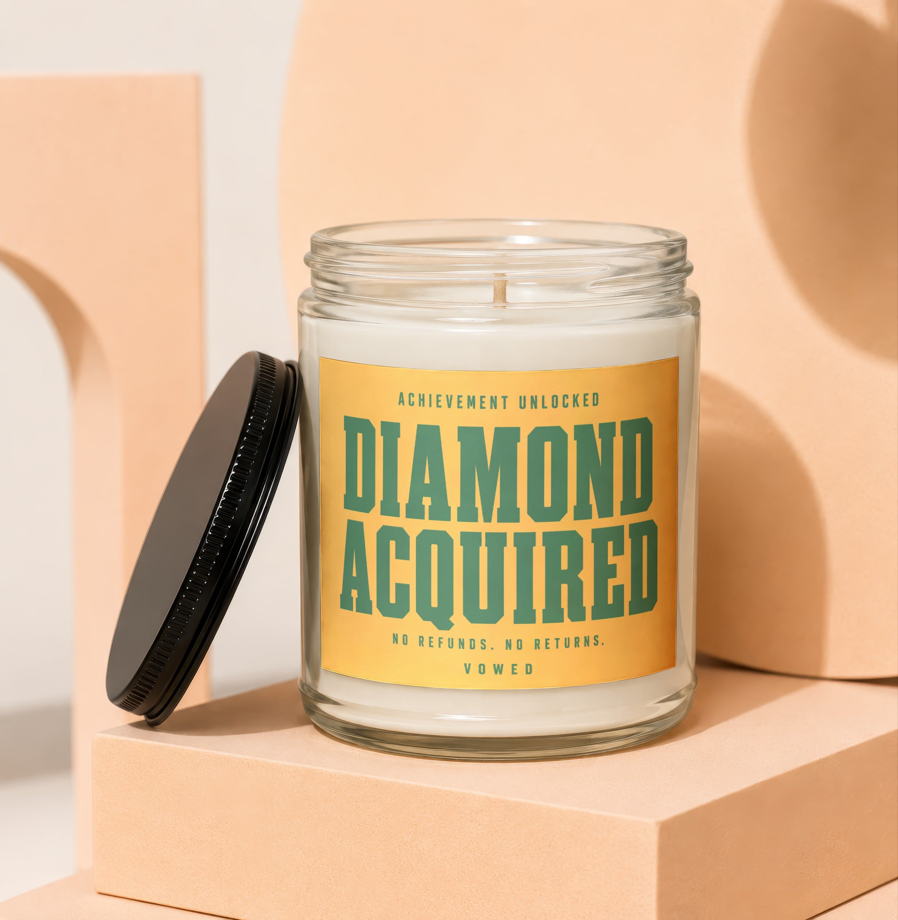Glass candle with yellow label: "Achievement Unlocked, Diamond Acquired, No Refunds. No Returns. Vowed."