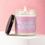 Glass jar candle with a lit wick, featuring a pink label with "Two people, one great love" in light blue script.