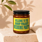 Amber jar candle with yellow label reading "Welcome to the Group Project Wedding Party"