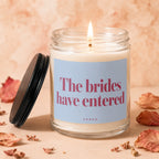 Candle with lit wick and "The brides have entered" text on a pale blue label.