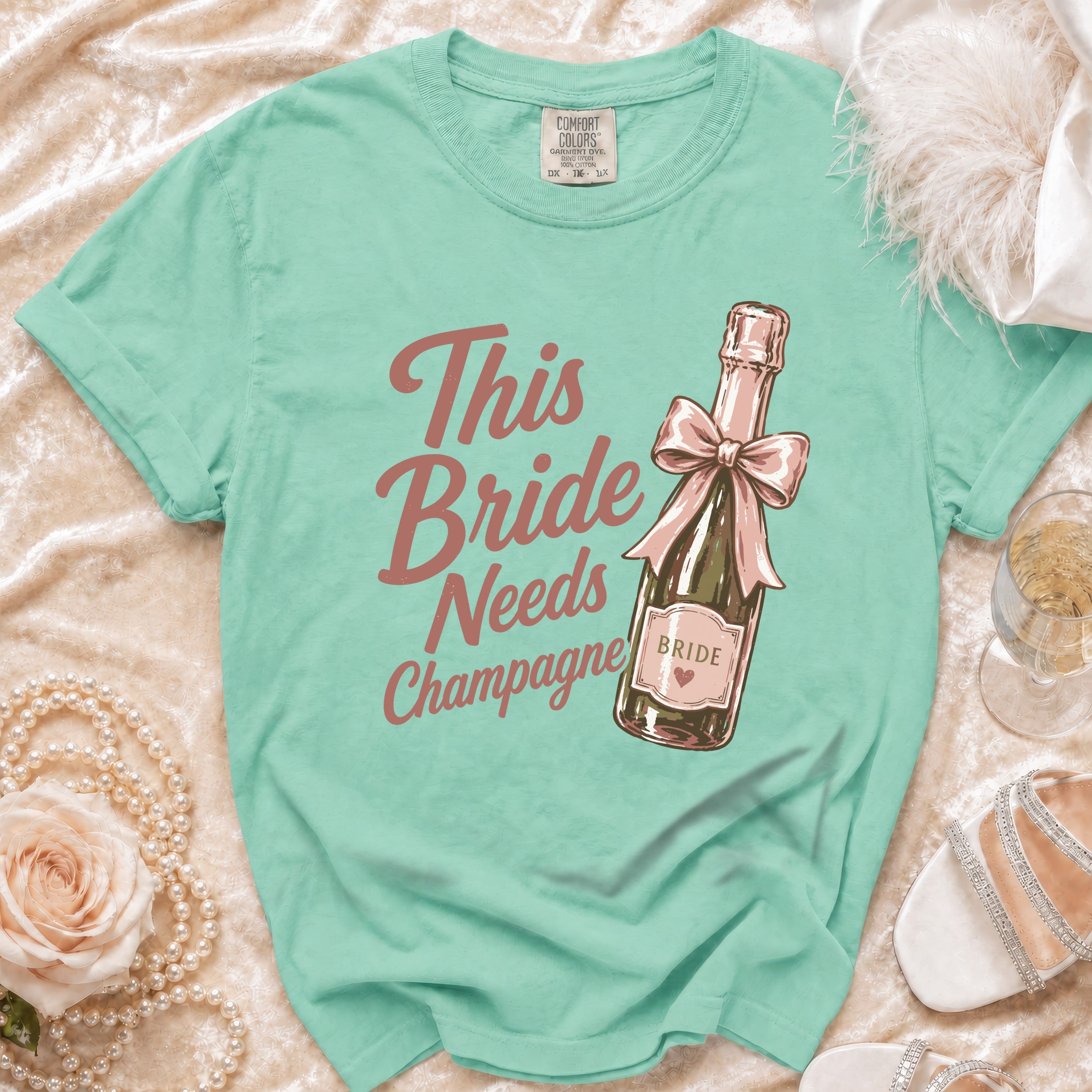 Teal t-shirt with "This Bride Needs Champagne" and a champagne bottle graphic.