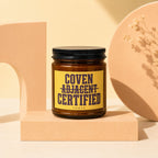 Amber jar candle with "Coven Adjacent Certified Vowed" on a yellow label.