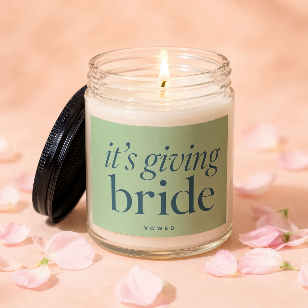 Candle with "it's giving bride" text on a green label, surrounded by pink petals.