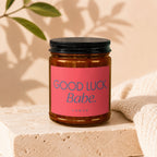Amber jar candle with pink label that reads "GOOD LUCK, Babe."