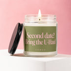 Glass jar candle with a lit wick and a black lid, featuring the text "Second date? Bring the U-Haul".