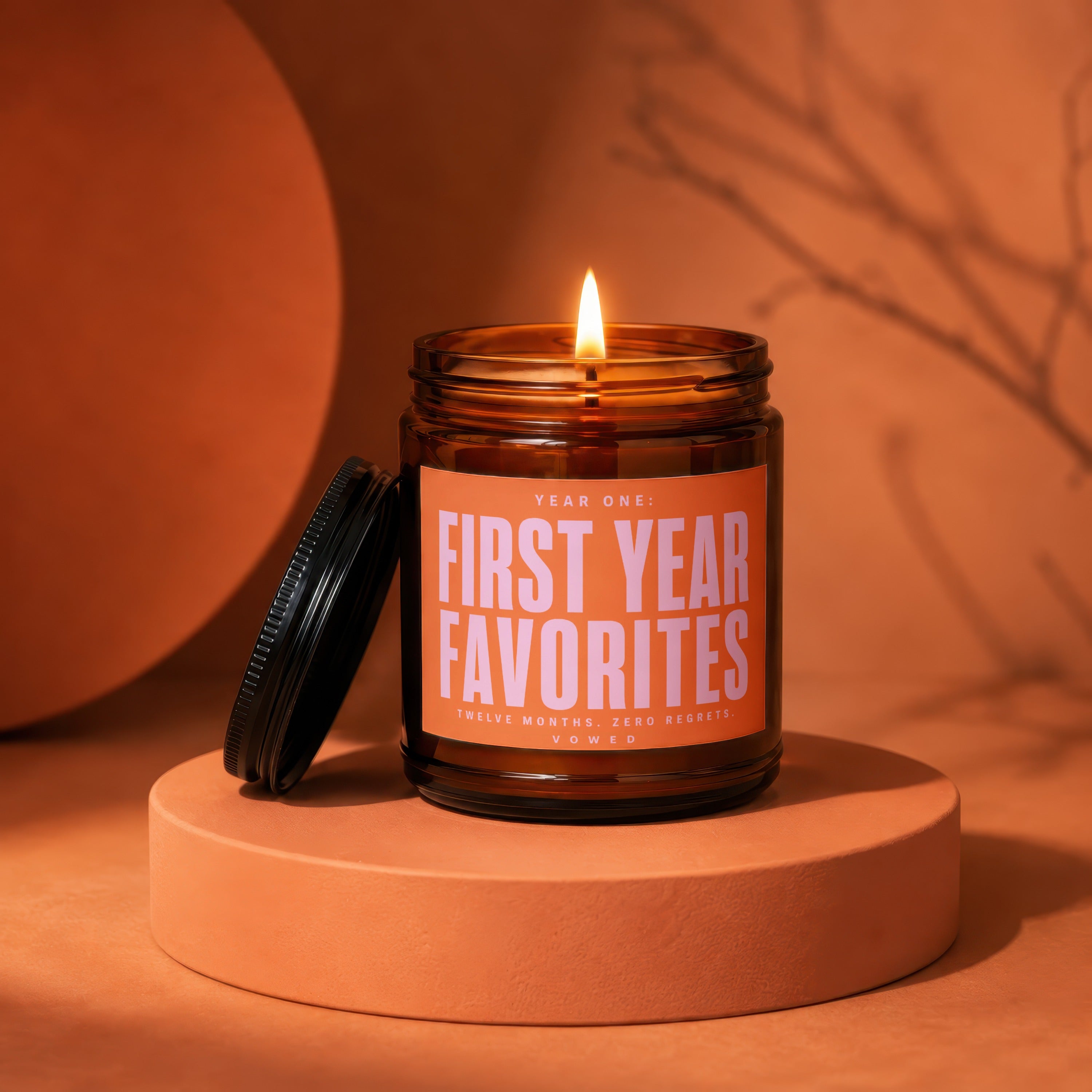 Amber jar candle with lit flame, "Year One: First Year Favorites" printed on label.