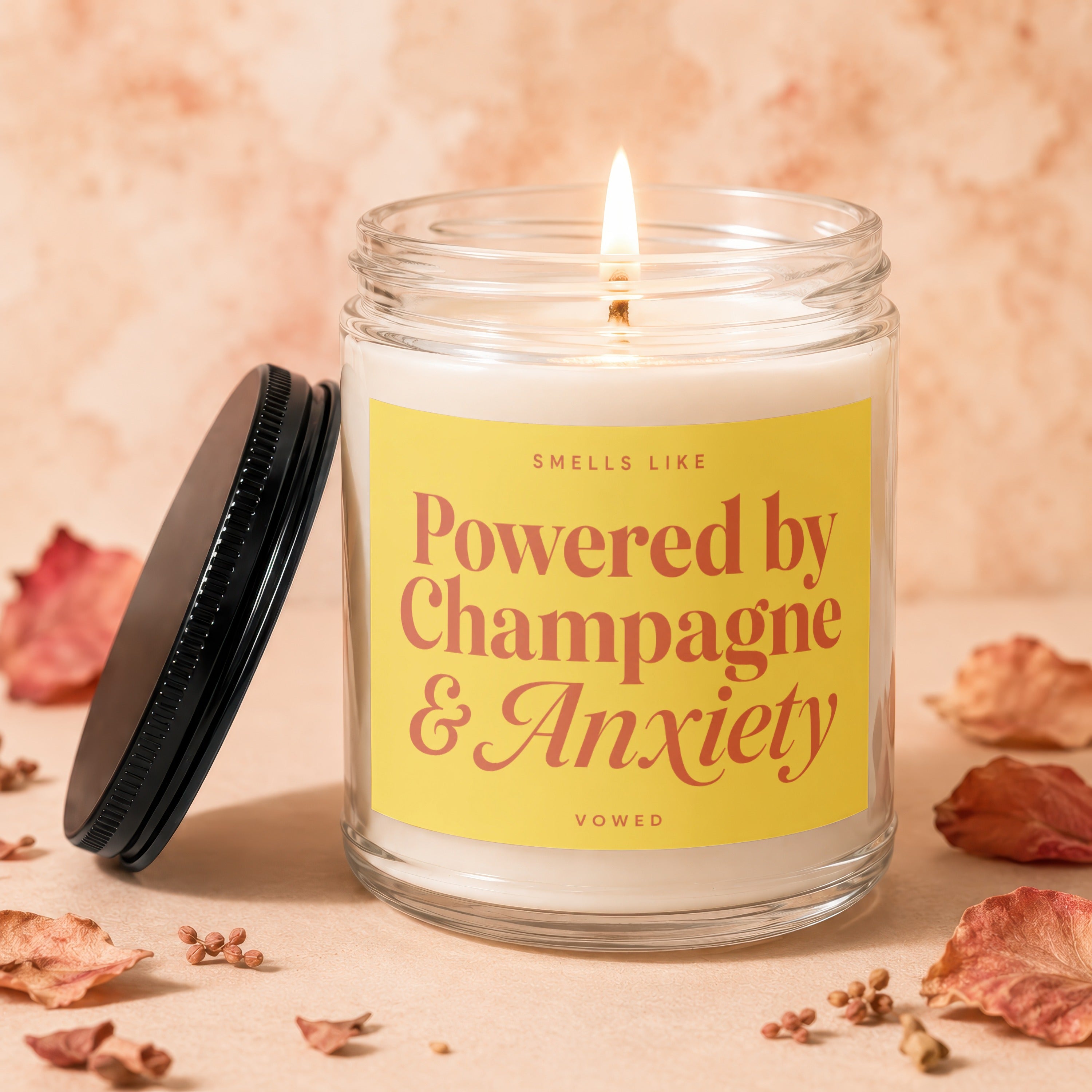 Candle labeled "Smells Like Powered by Champagne & Anxiety" with burning wick.