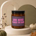 Brown glass candle with purple label reading "Love Never Feared The Dark".