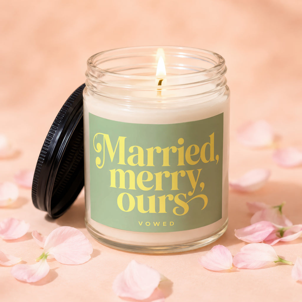 Lit candle in glass jar with "Married, merry, ours" text and pink petals.
