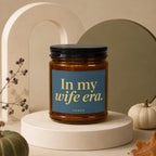 Brown candle with black lid, featuring "In my wife era. VOWED" text.