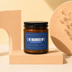 Amber glass candle with a blue label reading "He Married Up."