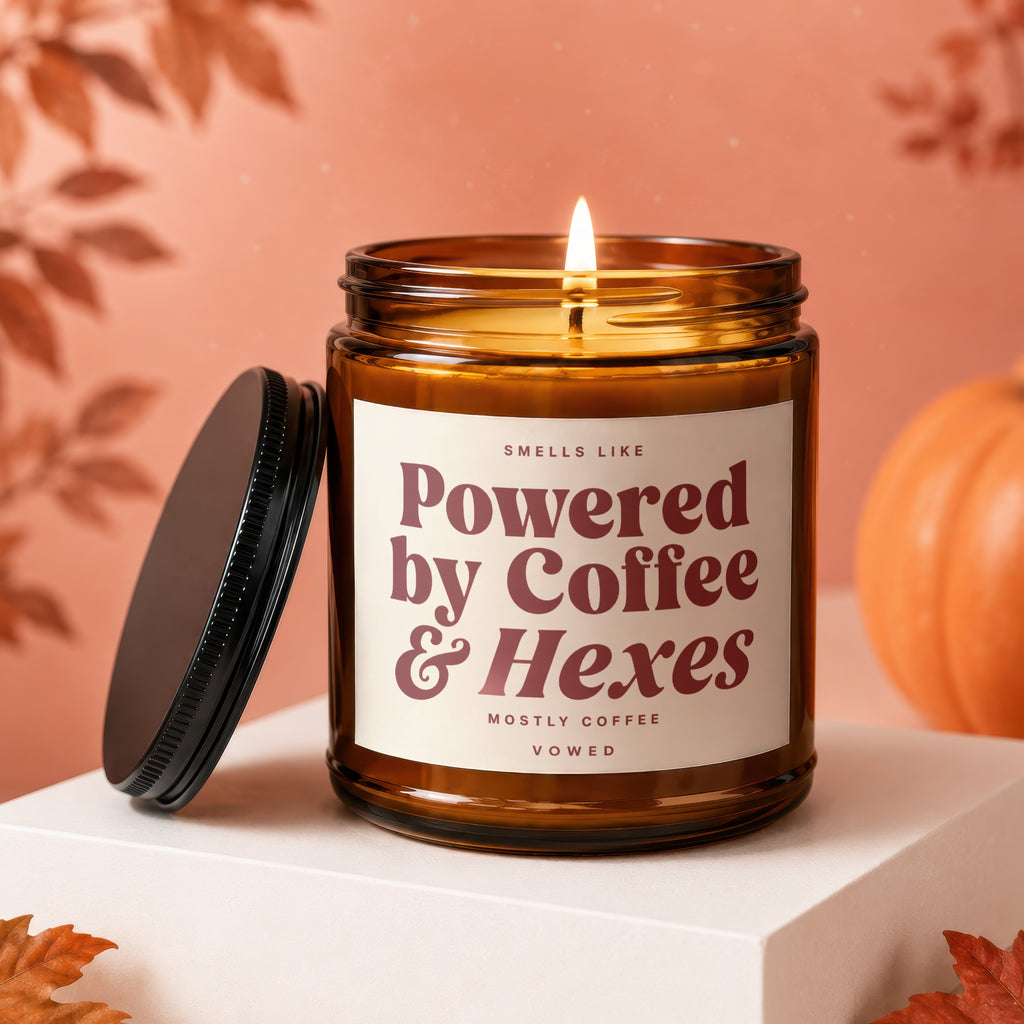 Brown glass candle with lit wick and "Powered by Coffee & Hexes" label.