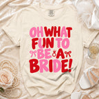 Cream t-shirt featuring pink and red text reading Oh What Fun To Be A Bride with bow and ring graphics.
