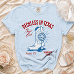Light blue t-shirt with "Reckless in Texas" and boot graphic.