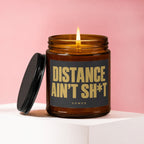 Amber jar candle with lid off and lit flame, displaying text "DISTANCE AIN'T SH*T".