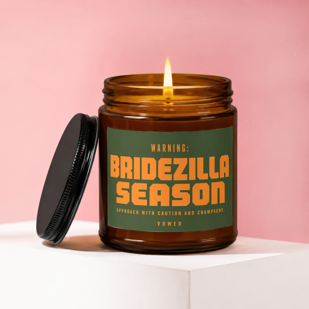 Amber glass candle with lit flame and green label reading "WARNING: BRIDEZILLA SEASON APPROACH WITH CAUTION AND CHAMPAGNE. VOWED".