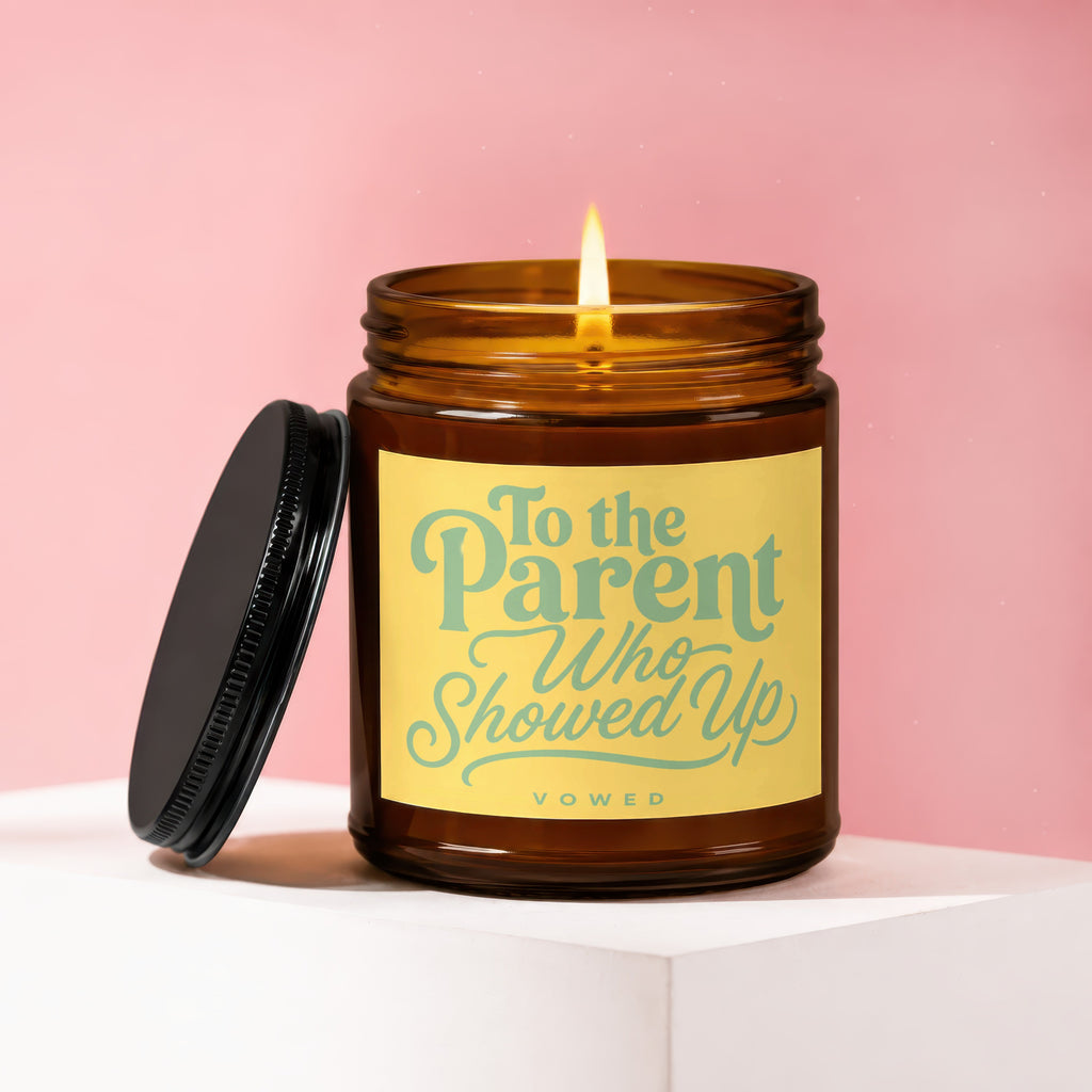 Amber jar candle with lit flame, featuring a yellow label that reads "To the Parent Who Showed Up."