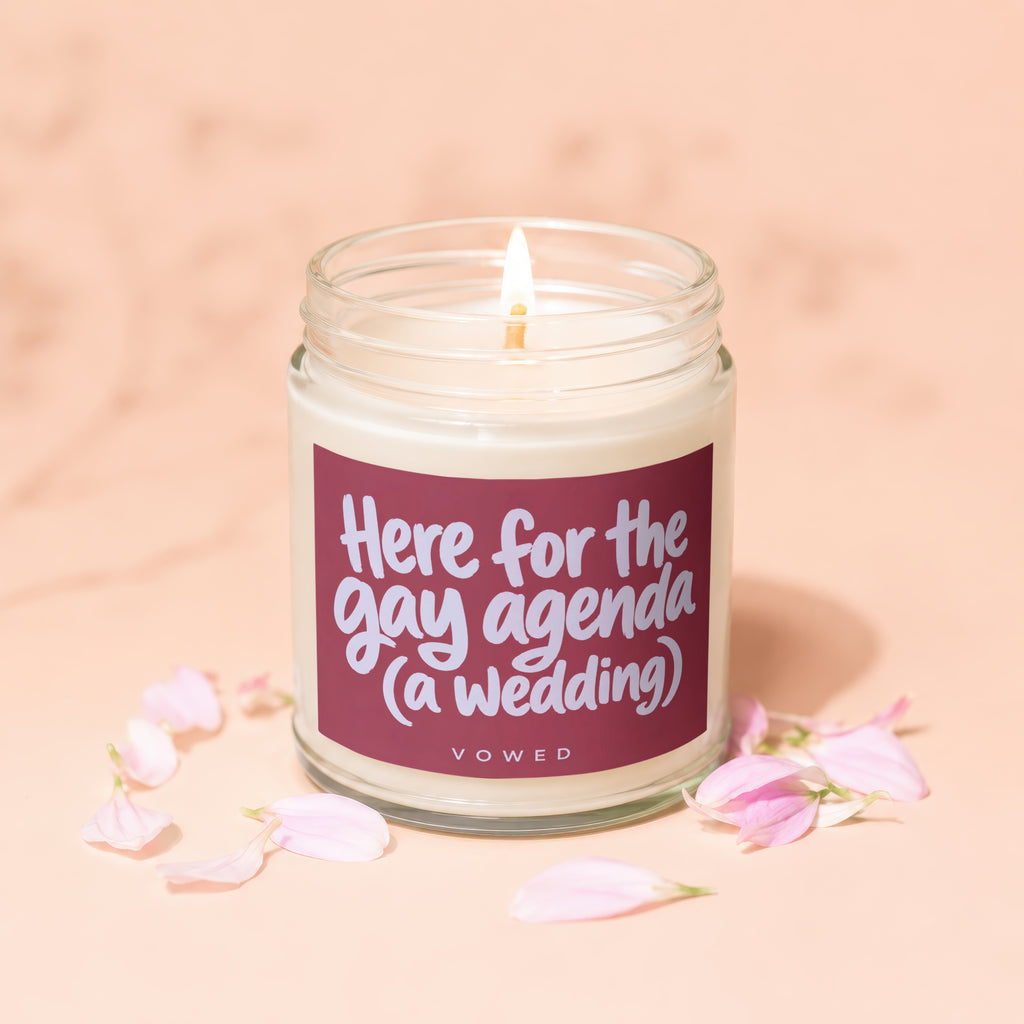 Candle with "Here for the gay agenda (a wedding)" text, surrounded by pink petals.
