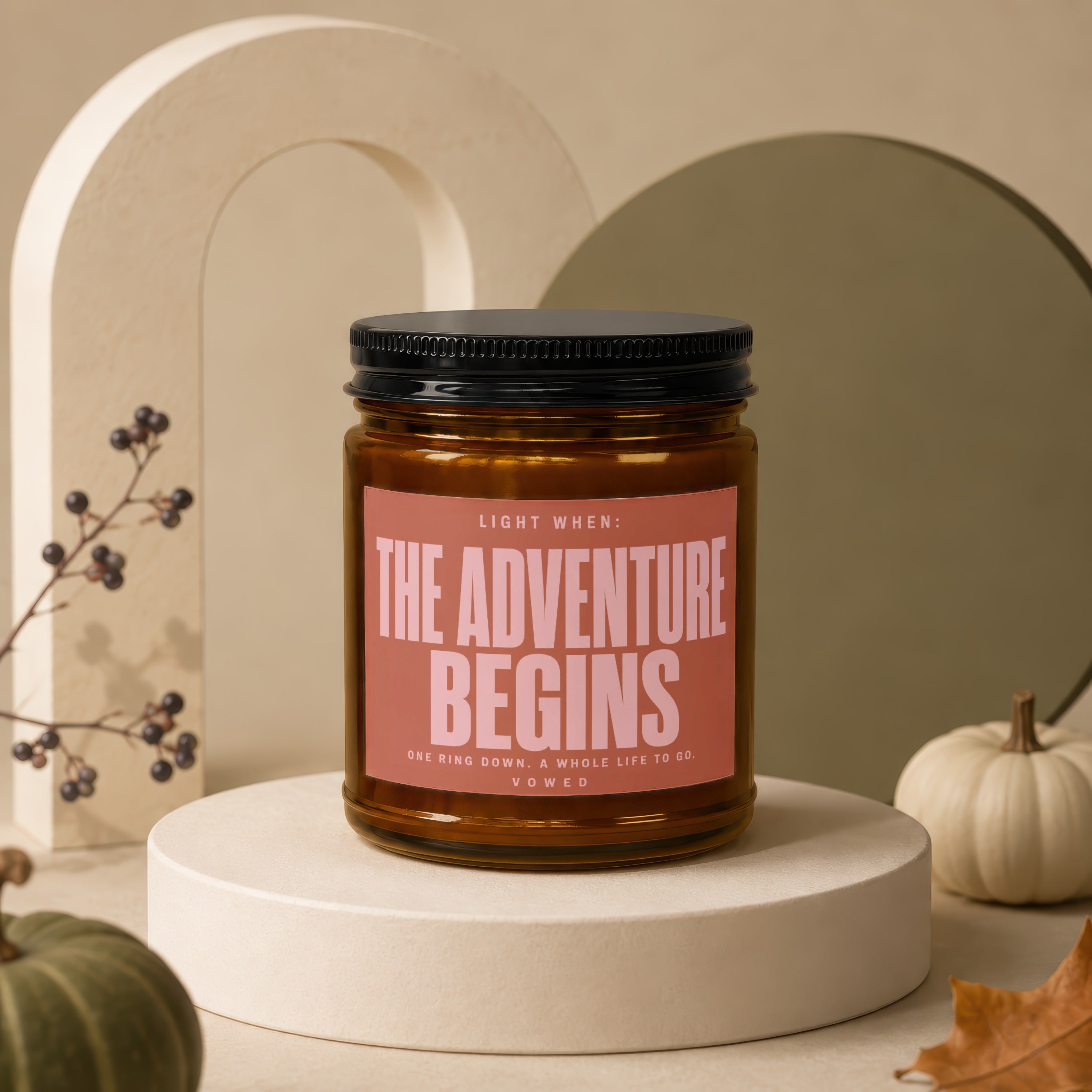 Amber jar candle with pink label reading "The Adventure Begins".
