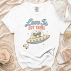 White t-shirt with aliens in a UFO, text "Love Is OUT THERE".