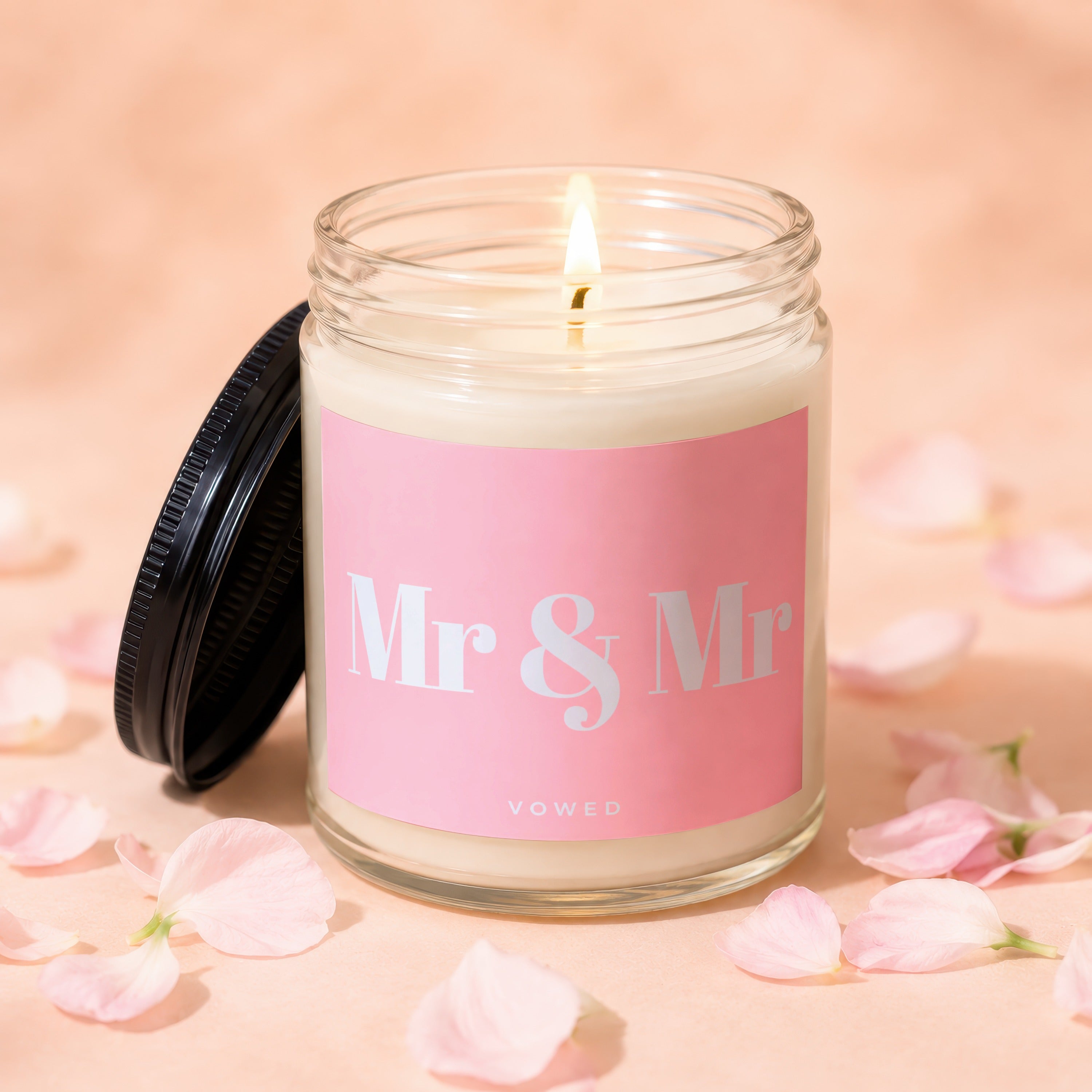 Candle with pink label reading "Mr & Mr VOWED", lit wick, surrounded by pink petals.