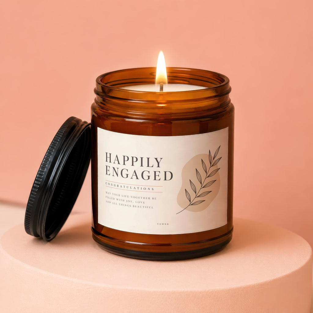 Candle with "Happily Engaged" text, lid open, on a pink pedestal.