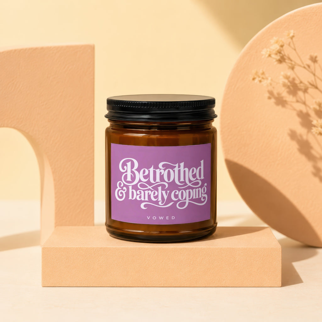 Amber jar candle with "Betrothed & barely coping" and "VOWED" text on purple label.