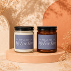 Two candles with black lids, one in clear glass, one in amber glass, labeled "In Memory of My Free Time".