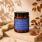 Glass candle with blue label reading "now act surprised like you didn't know this was coming. VOWED."