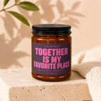Amber jar candle with dark lid reads "LOCATION: TOGETHER IS MY FAVORITE PLACE. NO TRAVEL REQUIRED."