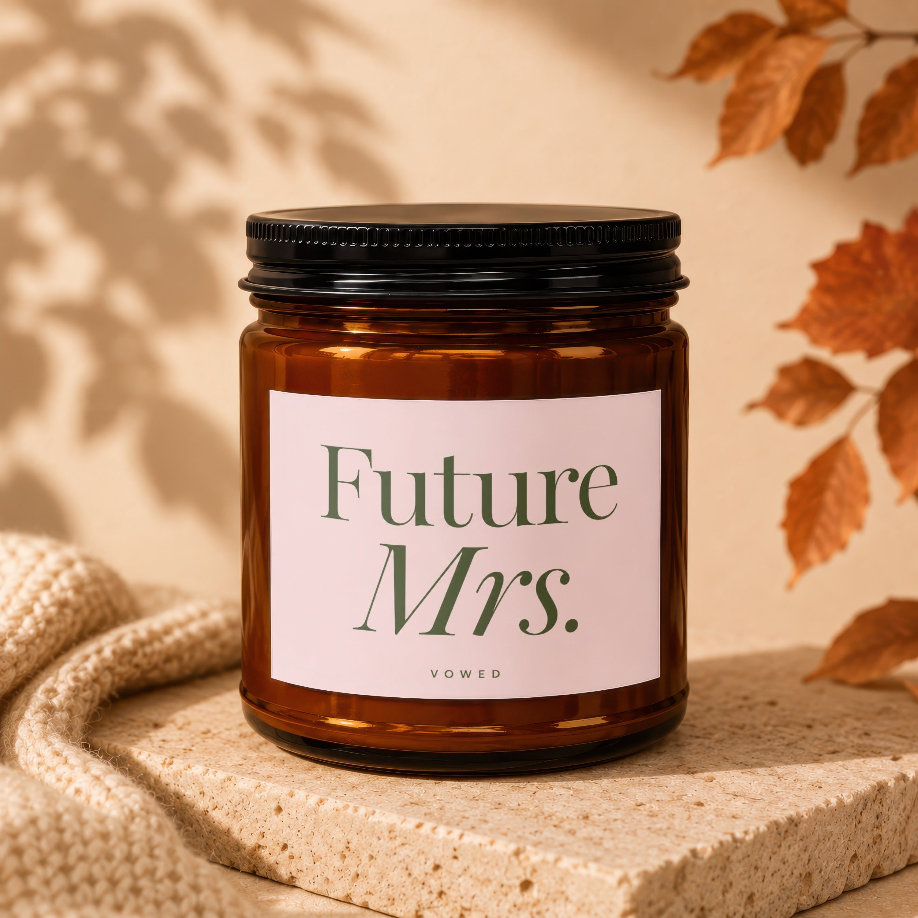 Amber candle with black lid labeled "Future Mrs. VOWED," set on stone.