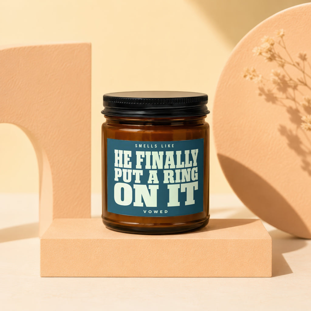 Amber jar candle with label reading "SMELLS LIKE HE FINALLY PUT A RING ON IT VOWED".