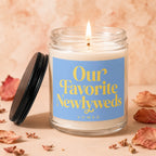Lit candle in a jar with blue label reading "Our Favorite Newlyweds VOWED".