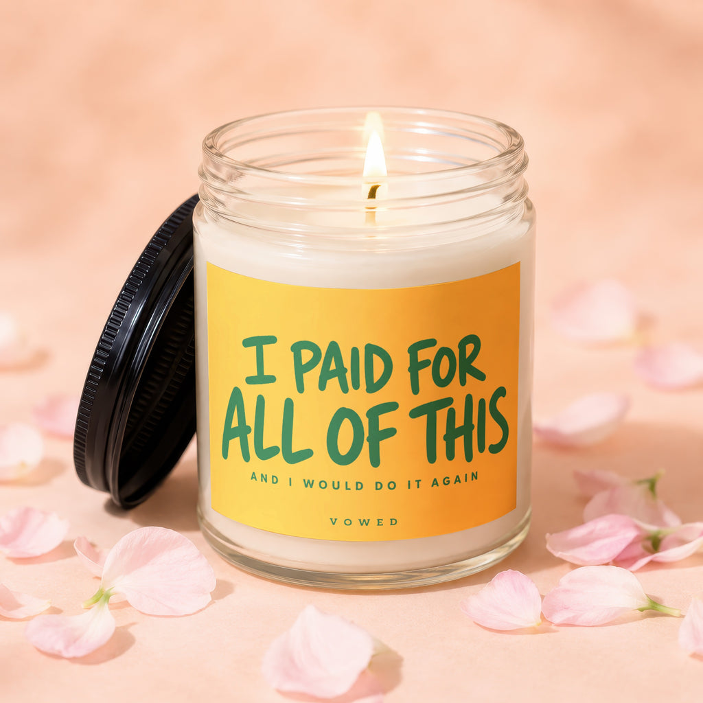 Lit candle in a glass jar with yellow label saying "I PAID FOR ALL OF THIS AND I WOULD DO IT AGAIN".