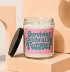 Glass jar candle with pink label reading "Surviving Celebrating Forever"