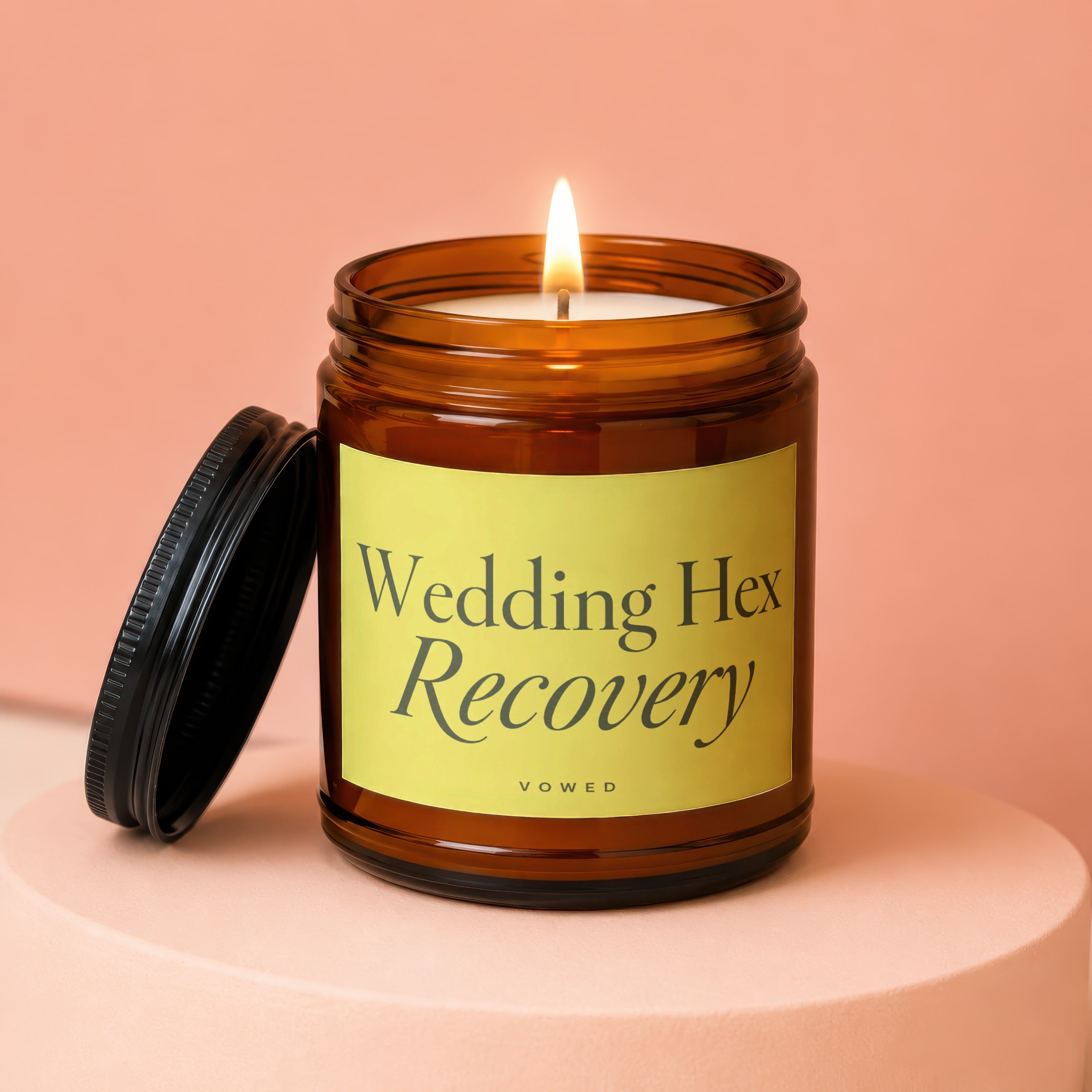 Amber candle with lit wick and black lid, reads "Wedding Hex Recovery VOWED".